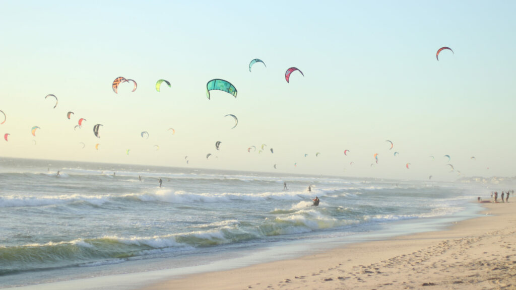 Das Bild von Kitesurfern am Strand symbolisiert die Dynamik im B2B-Sektor, insbesondere im Umgang mit Kundenbindung und -abwanderung. Es verdeutlicht die Notwendigkeit für Unternehmen, agil zu bleiben und sich an die sich ändernden Kundenbedürfnisse anzupassen, um Kundenbindung zu stärken und Abwanderung zu minimieren.
